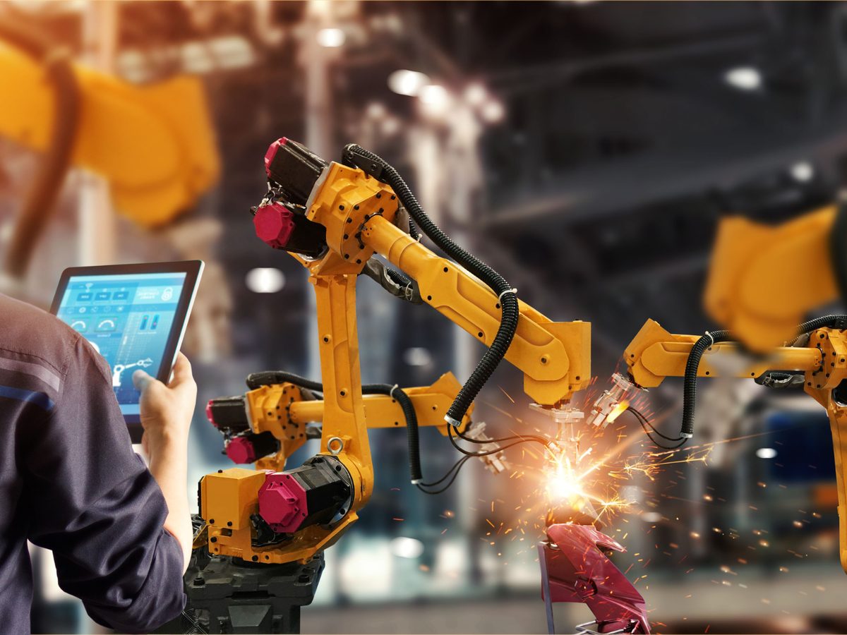 Mitarbeiter mit Tablet steuert Industrieroboter in einer Produktionshalle